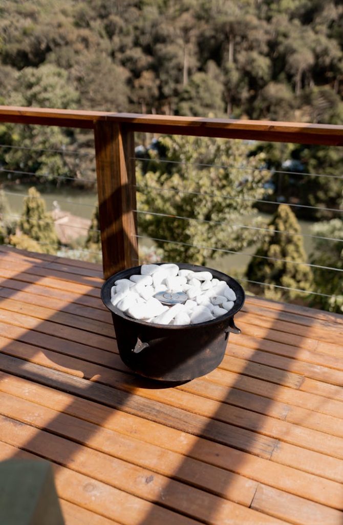 Round fire pit with white rocks on a wooden balcony overlooking a forest view.